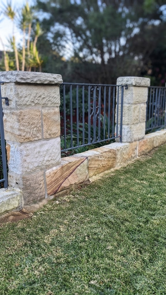 Sandstone garden wall and iron fence bordering a neatly maintained lawn